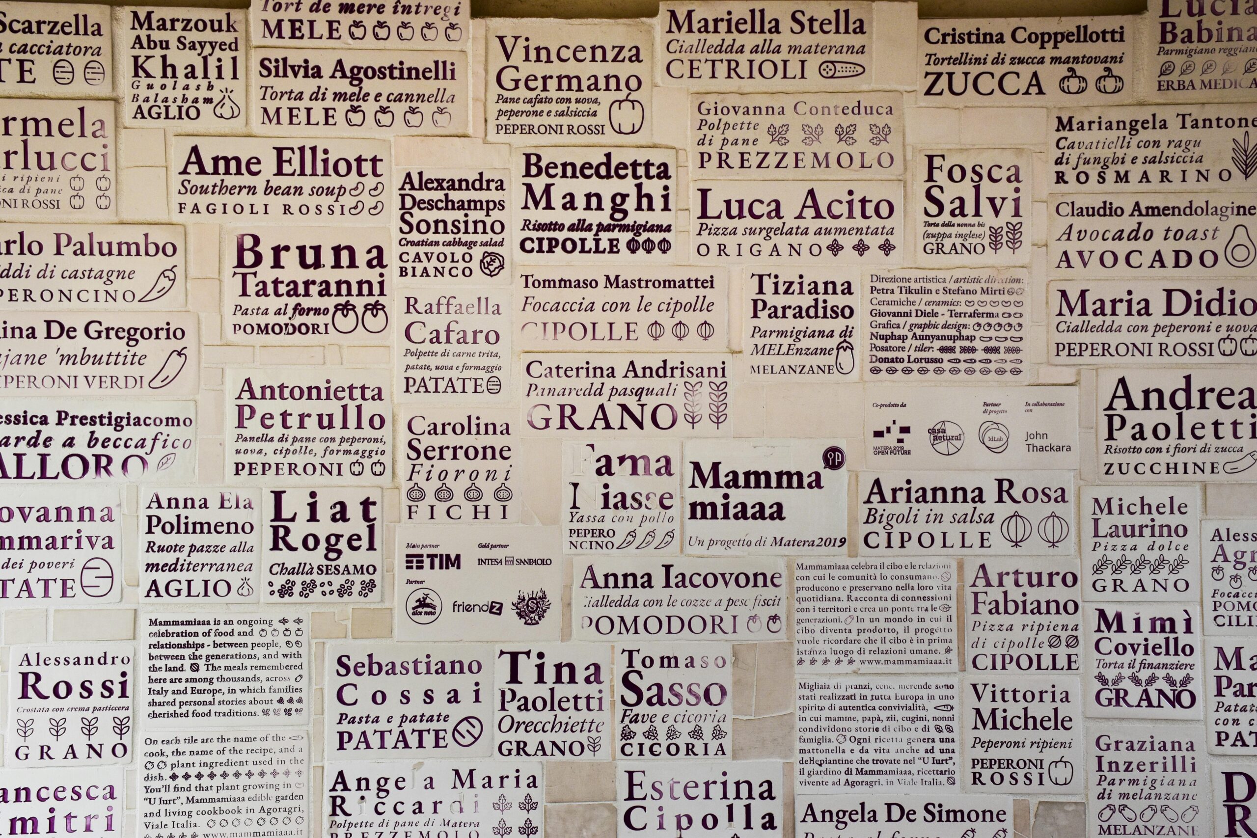 Wall of artisan tiles showcasing local names and recipes in Matera, Apulia.